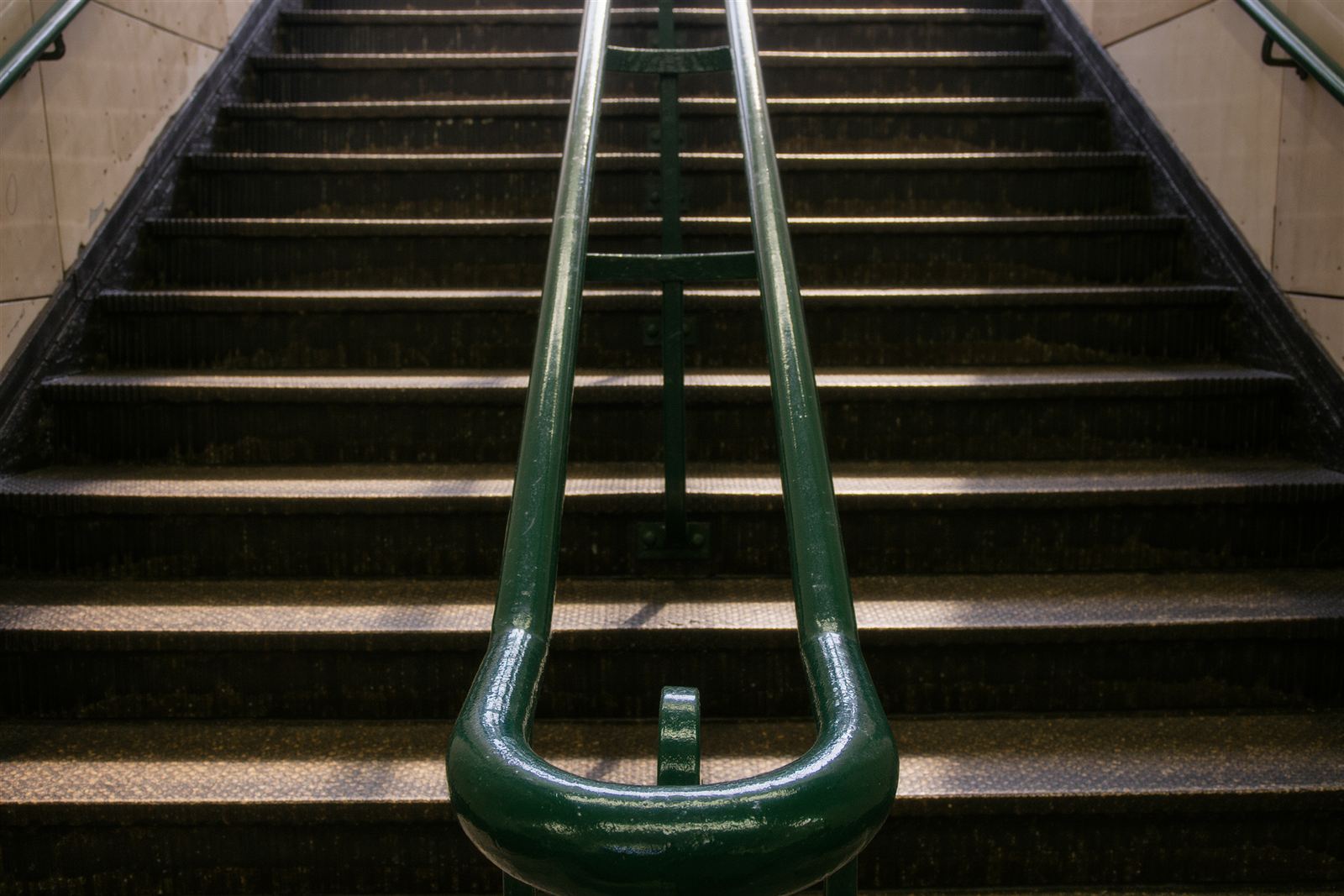 A green iron handrail on a worn subway stairway in evening light