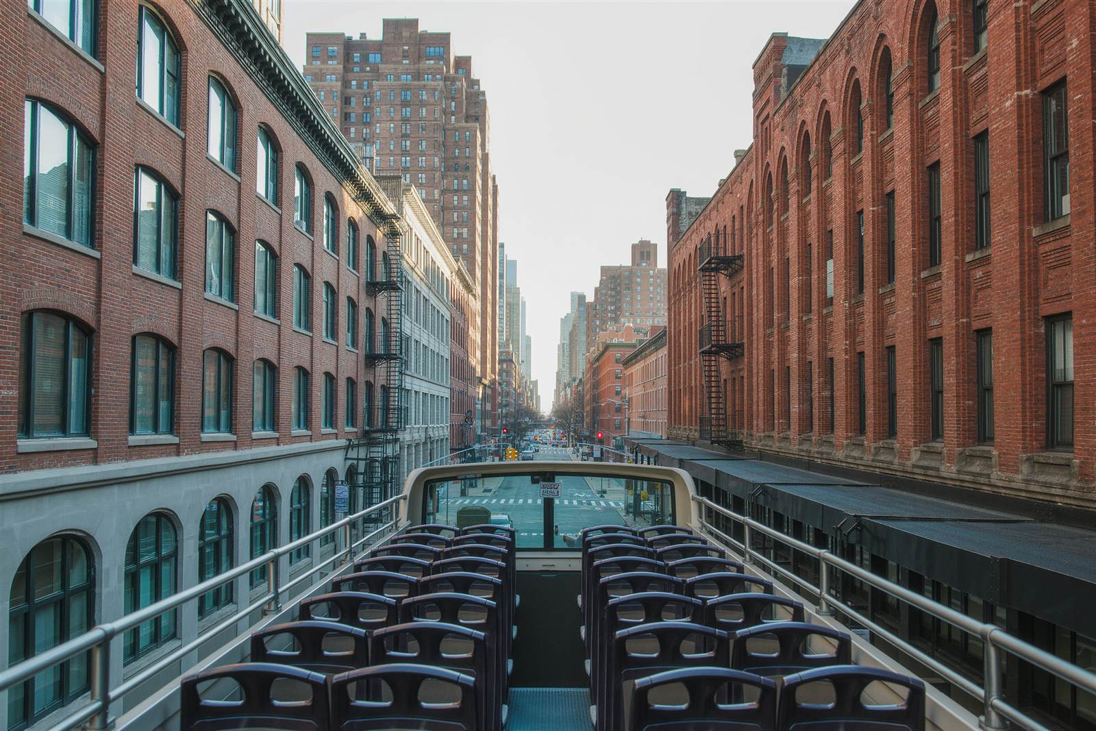 Empty seats on the upper deck of an open-top sightseeing coach between brick buildings