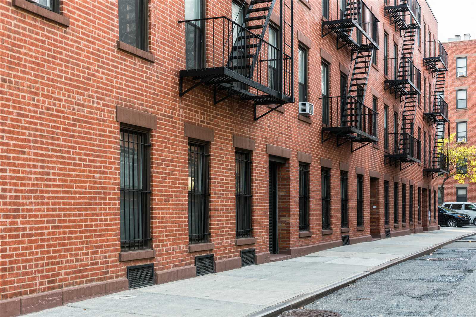 Red-brick apartment buildings with black fire escapes on a quiet street