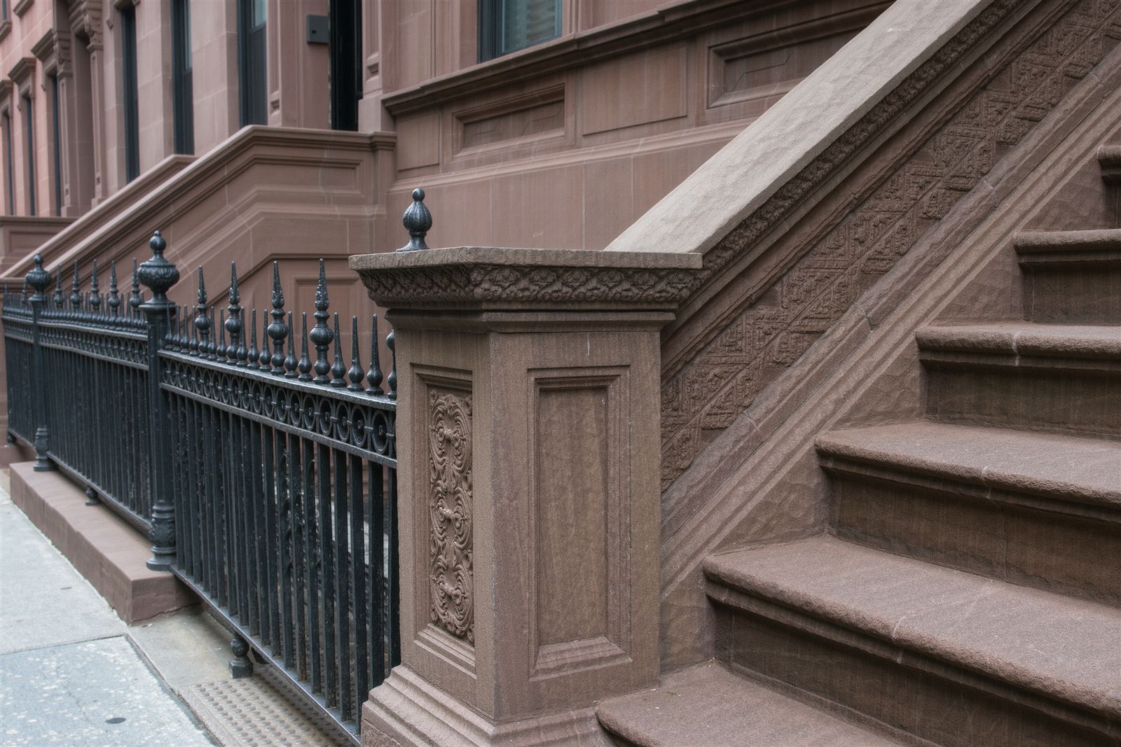 A carved brownstone newel post, stone steps and a wrought-iron fence on a Harlem street