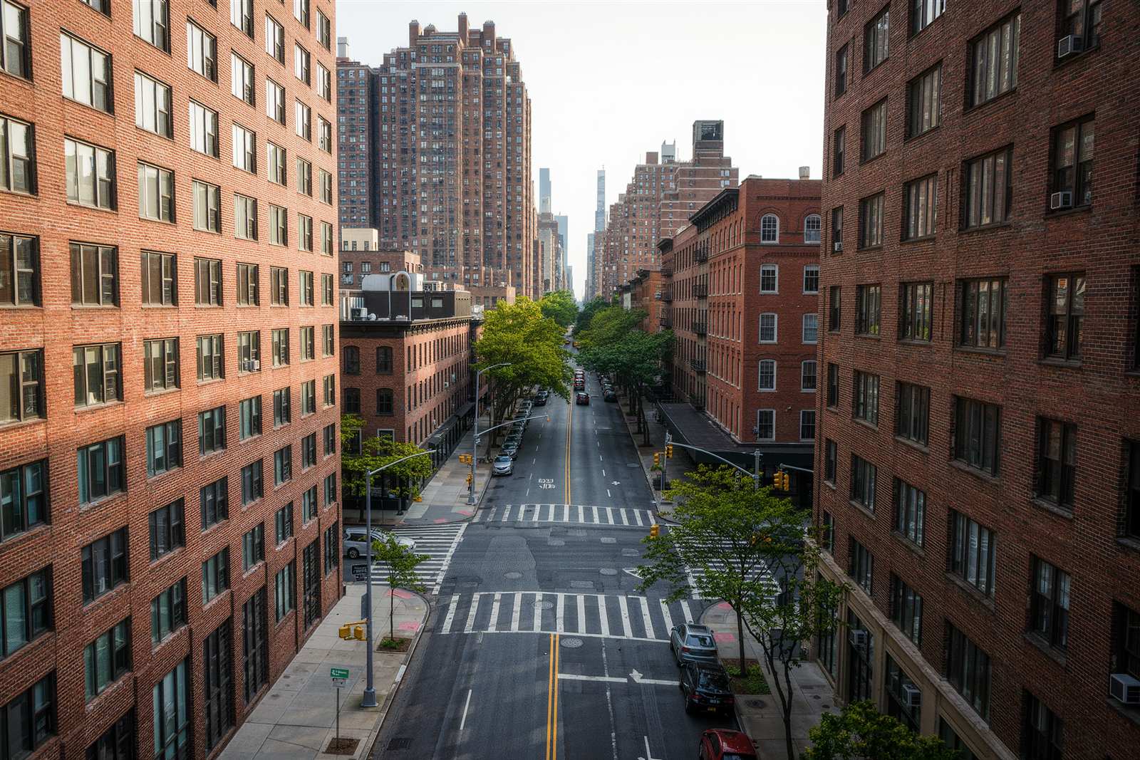 A city street seen from above between rows of brick buildings and street trees